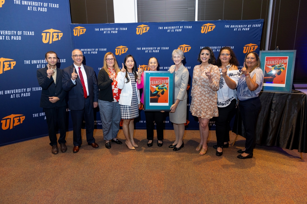 A group of attendees poses with framed artwork in front of a UTEP backdrop.
